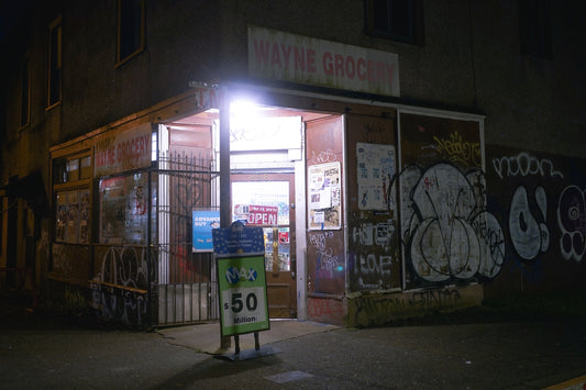 Corner grocery store at night with graffiti on wall.